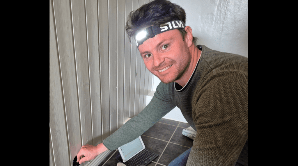 Takstmann Jan Martin Rønning gjennomfører fuktmåling i en vegg ved hjelp av et inspeksjonshull, iført hodelykt og med måleverktøy klart.