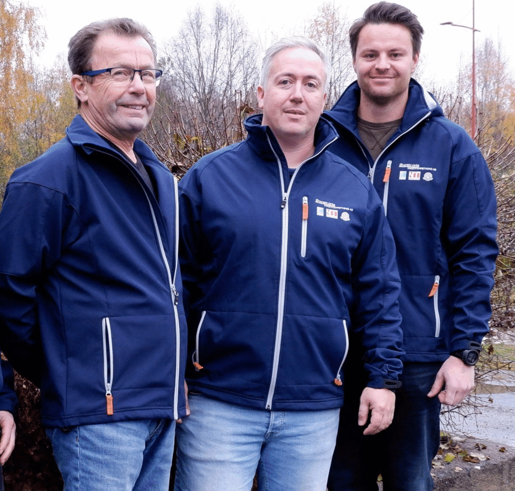 Teamet i Øystein Opås Takstforretning står utendørs i firmajakker og smiler mot kamera, med høstfargede trær i bakgrunnen.