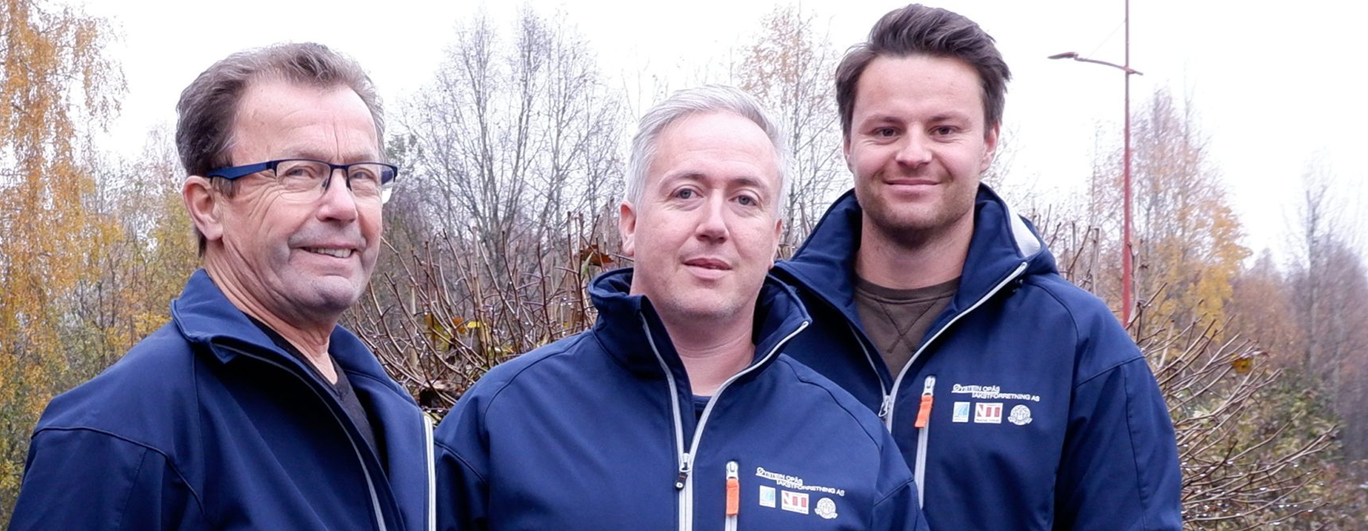 Teamet i Øystein Opås Takstforretning står utendørs i firmajakker og smiler mot kamera, med høstfargede trær i bakgrunnen.